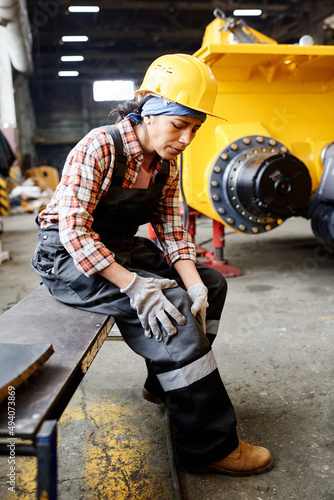 Obraz na plátně Young female engineer in protective helmet and coveralls sitting on bench and to