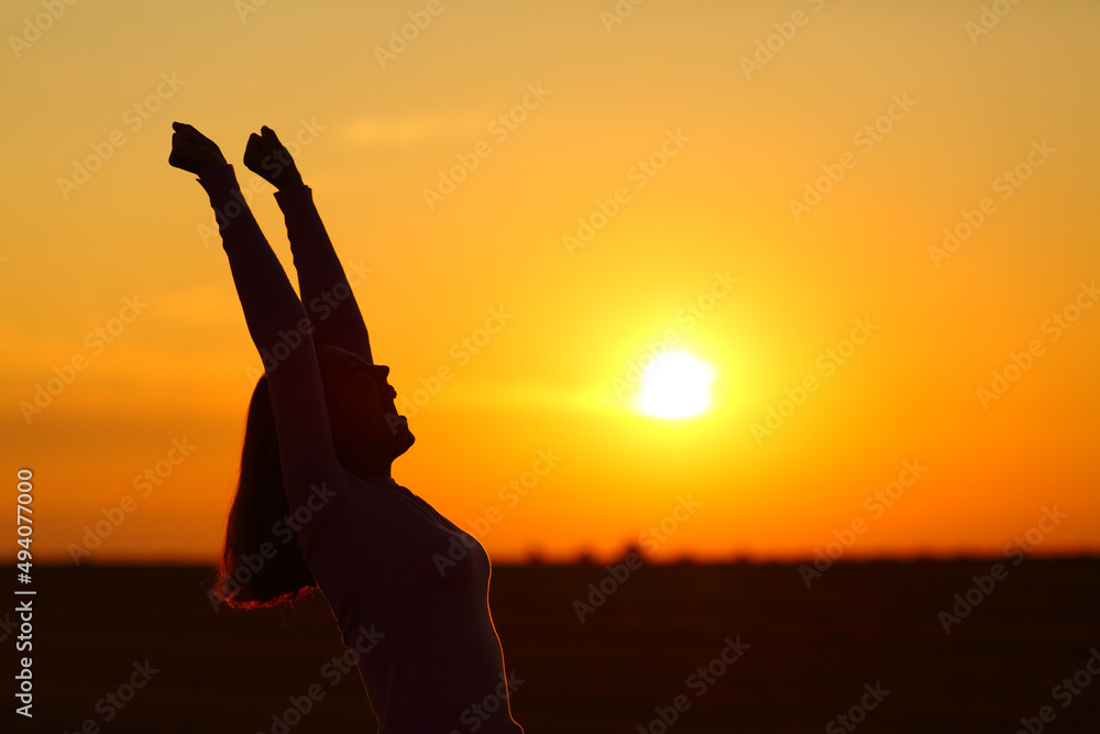 Excited woman raising arms celebrating at sunrise