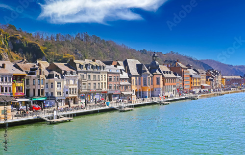 Dinant, Belgium - March 9. 2022: View over river meuse on waterfront promenade with ancient colorful houses against blue winter sky, fluffy clouds © Ralf