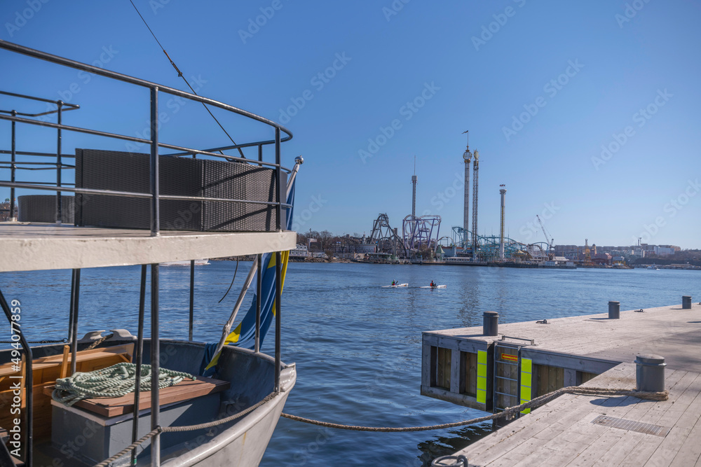 Stern of a motor yacht at a jetty, canoes passing at the waterfront of the island Djurgården a sunny spring day in Stockholm