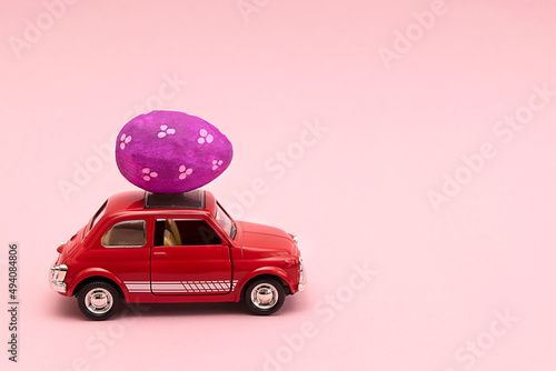 Minsk, Belarus - Marth 2022: Easter holiday. A red toy car with colorful eggs on pink background.