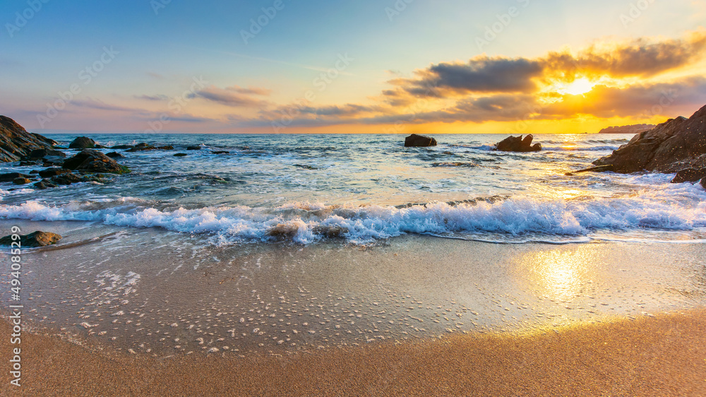 summer vacation at the beach. idyllic seascape at sunrise. calm waves washing the shore with sand and rocks. sun behind the glowing cloud above horizon. meditation and relax concept