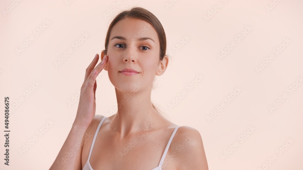 Young adult beauty model posing for skin care products commercial. Brunette woman touches her face and looks at camera against nude background Young adult beauty model posing for skin care products commercial. Brunette woman touches her face and looks at camera against nude background