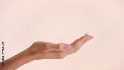 Close-up shot of a female hand with a drop of skin care cream on the top of her finger against nude background
