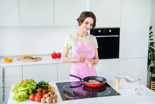 Photo of pretty peaceful lady frying fresh fish hold pepperbox add spices morning kitchen indoors photo
