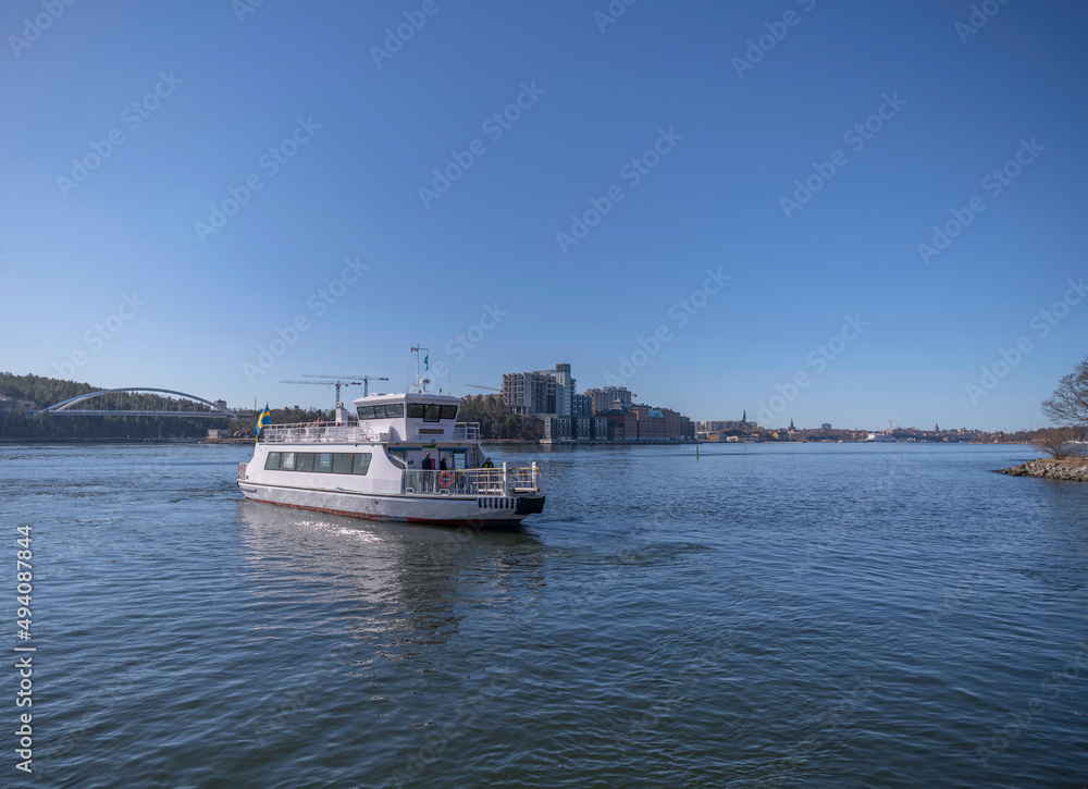 Commuting boat leaving a jetty with apartment houses as skyline a sunny spring day in Stockholm