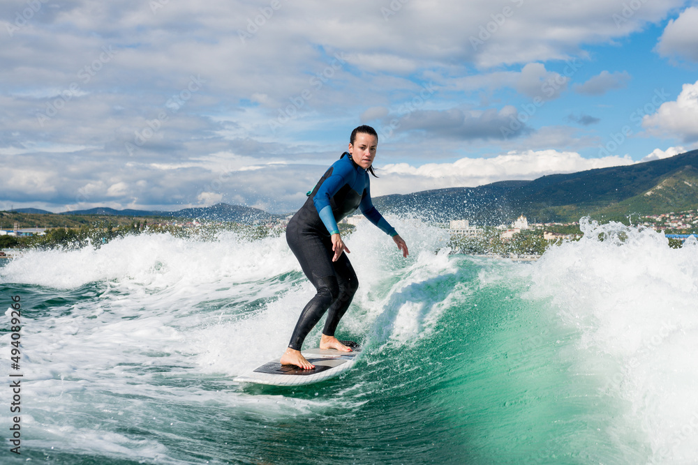 Young athletic female in wetsuit riding on endless waves behind a boat on sunny day. Woman practice wakeboarding, carving behind the baot. Watersport concept.