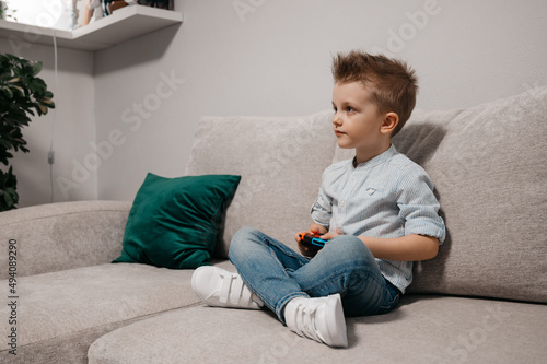 Happy boy playing video games holding game controller sitting on the coach in living room