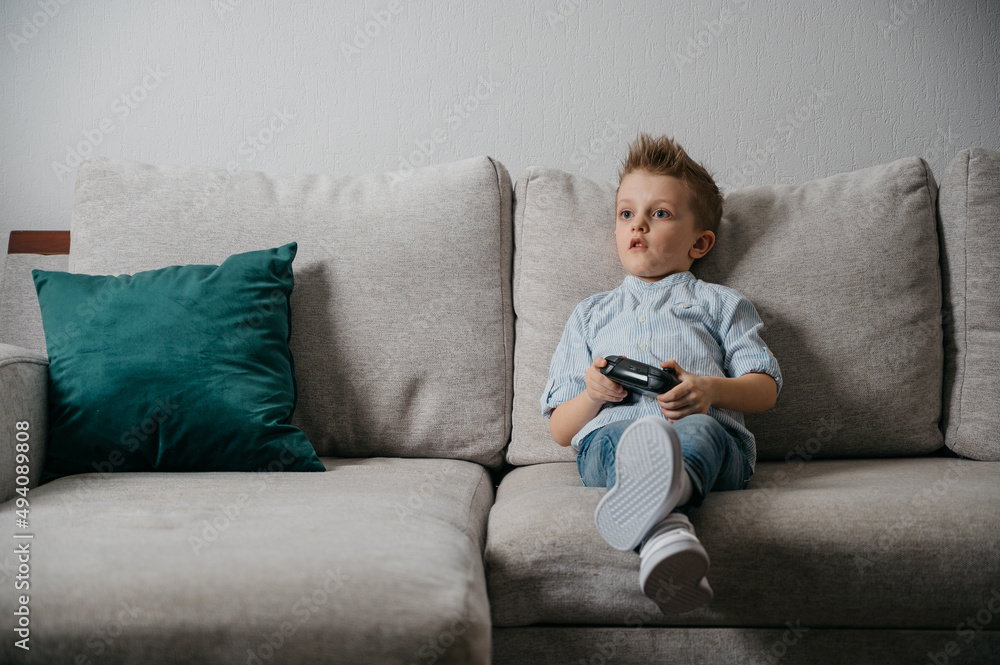 Happy boy playing video games holding game controller sitting on the coach in living room Happy boy playing video games holding game controller sitting on the coach in living room