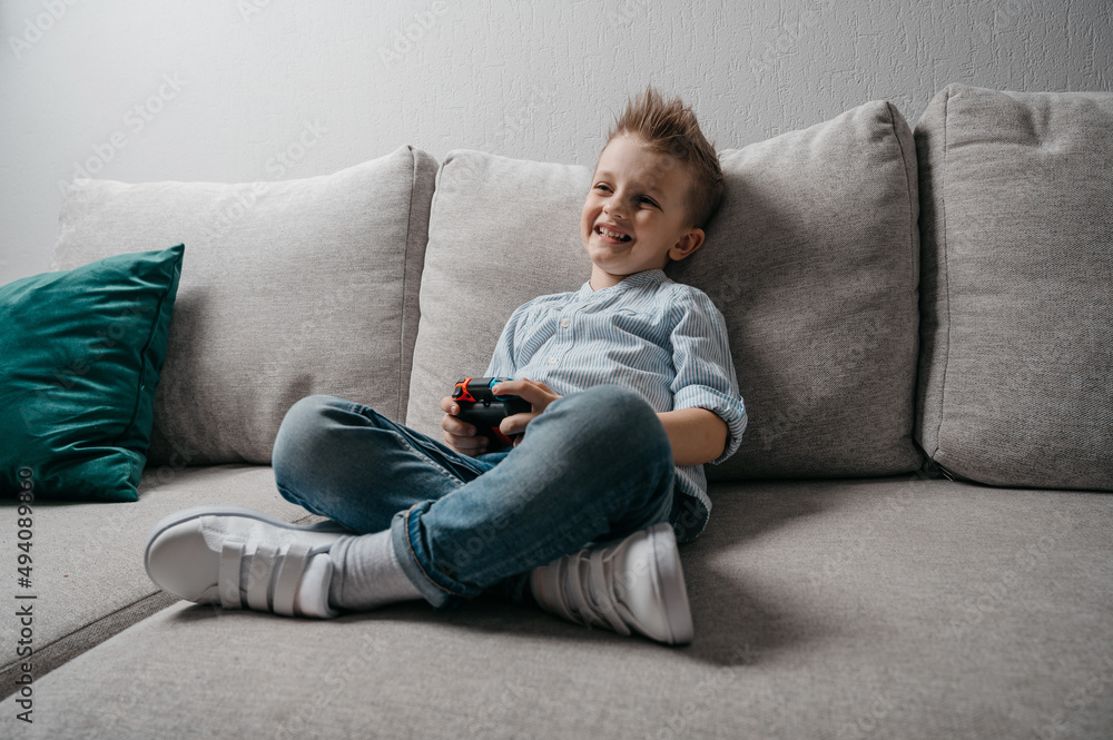 Happy boy playing video games holding game controller sitting on the coach in living room