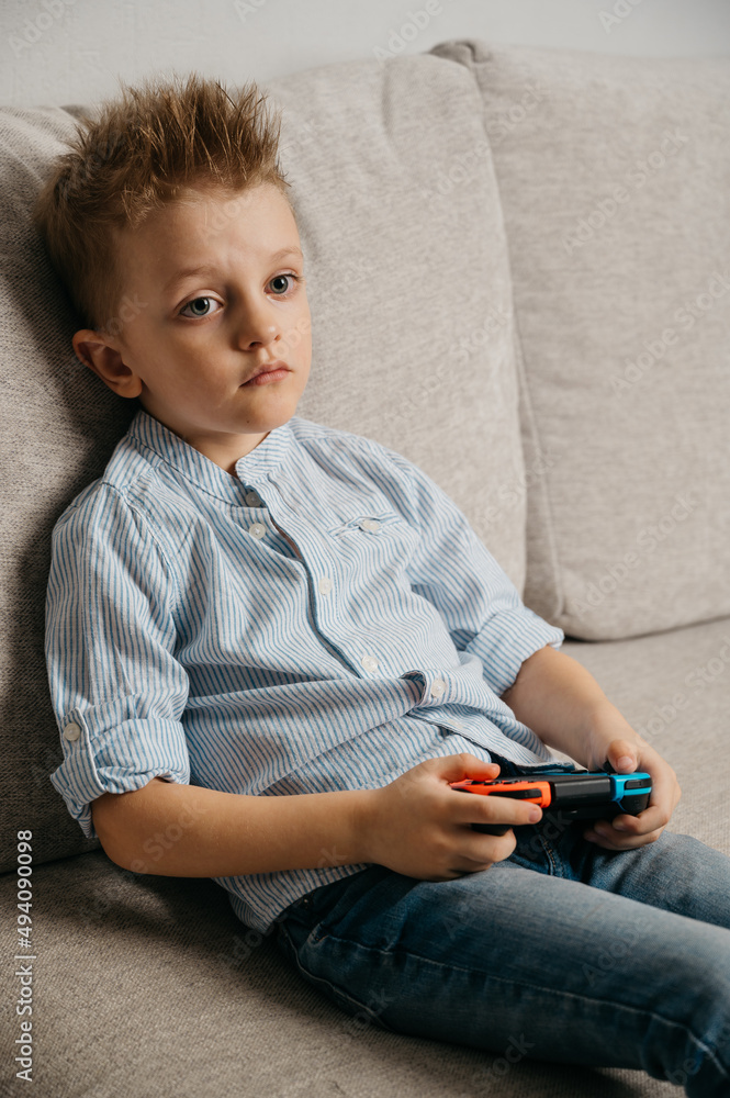 Happy boy playing video games holding game controller sitting on the coach in living room Happy boy playing video games holding game controller sitting on the coach in living room