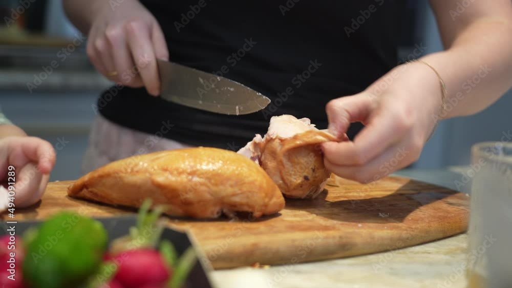 Woman removes the skin and cuts a tender smoked chicken with a knife on a cutting board in the kitchen at home Woman removes the skin and cuts a tender smoked chicken with a knife on a cutting board in the kitchen at home