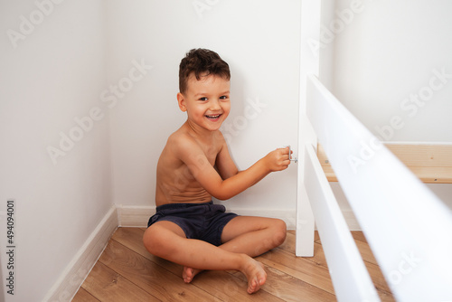 small child assembles furniture, children's craft concept, front view. the boy smiles as he assembles his new wooden bed.