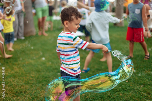 the child inflates large soap bubbles. Street animation program, happy child on a green lawn. Summer vacation. A boy in bright striped clothes with soap bubbles. Large portrait, horizontal.