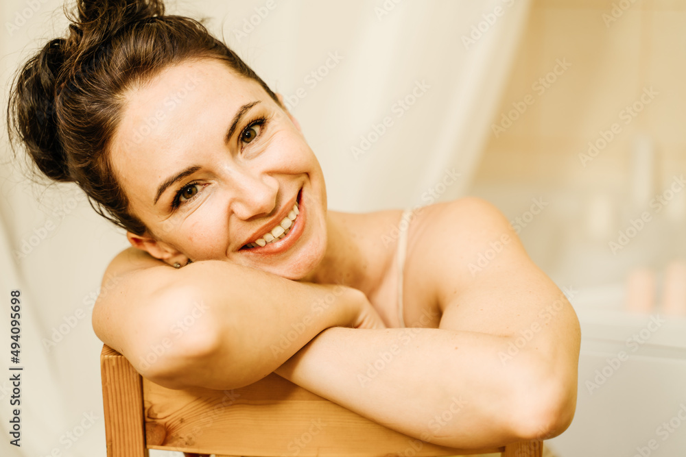 Portrait of a middle-aged woman, smiling with her arms folded in front of her face, her hair pulled up. The brunette is in a good mood. On a light background. Portrait of a middle-aged woman, smiling with her arms folded in front of her face, her hair pulled up. The brunette is in a good mood. On a light background.