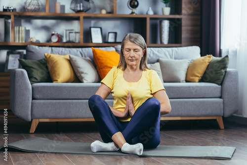 Older gray-haired woman at home alone, active lifestyle, yoga, lotus position and meditating