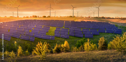solar panels field and wind turbines under blue sky on summer landscape, alte...