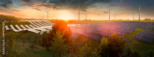 field of solar panels and wind generators at sunset, glare and reflections, b...