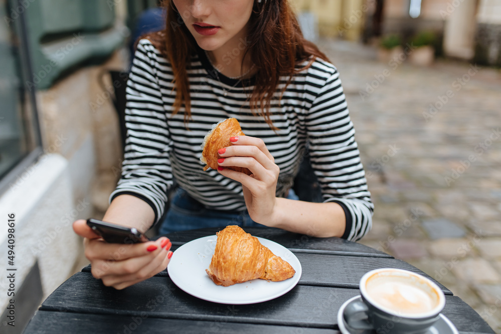 Woman using smartphone while eating croissant at cafe Woman using smartphone while eating croissant at cafe
