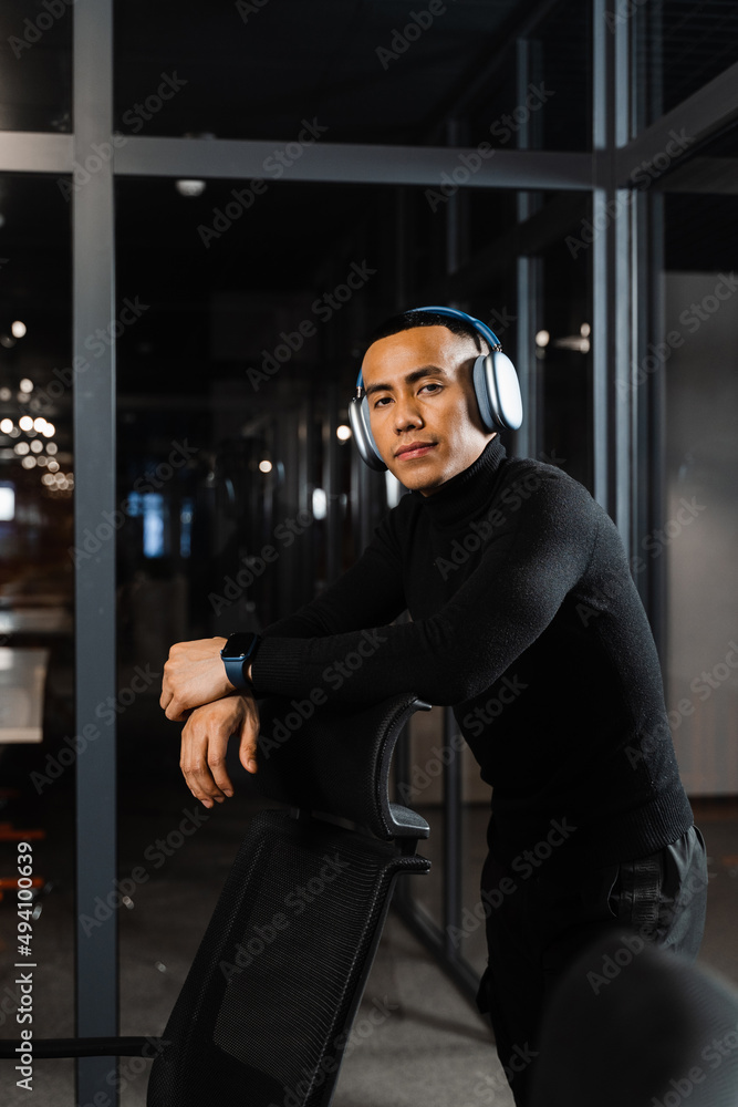 Asian man in headphones working online and listen to music in office. Asian handsome guy with laptop in coworking space.