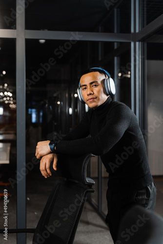 Asian man in headphones working online and listen to music in office. Asian handsome guy with laptop in coworking space.