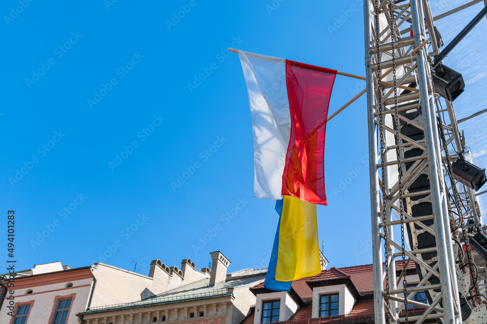 Flags of Ukraine and Poland on the metal arch of the stage on the square against the blue sky on a sunny day. Solidarity of Poland with Ukraine