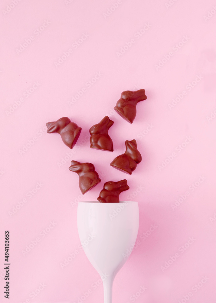 Chocolate bunnies going out of a white wine glass on pastel pink background. Surreal concept for Easter celebration banner or card.