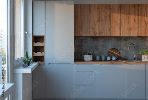 Modern interior of kitchen with stylish kitchen cabinets, counter and window. Tiles on the wall and kitchenware in new apartment.