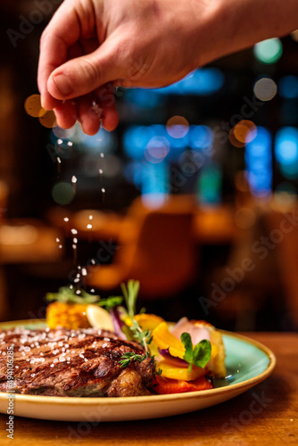 Fototapeta Naklejka Na Ścianę i Meble -  Plate of food with steak and vegetables in a restaurant being finished with sea salt by a chef
