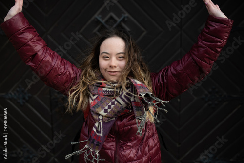 Happy young woman with Down syndrome with raised arms in town in winter photo