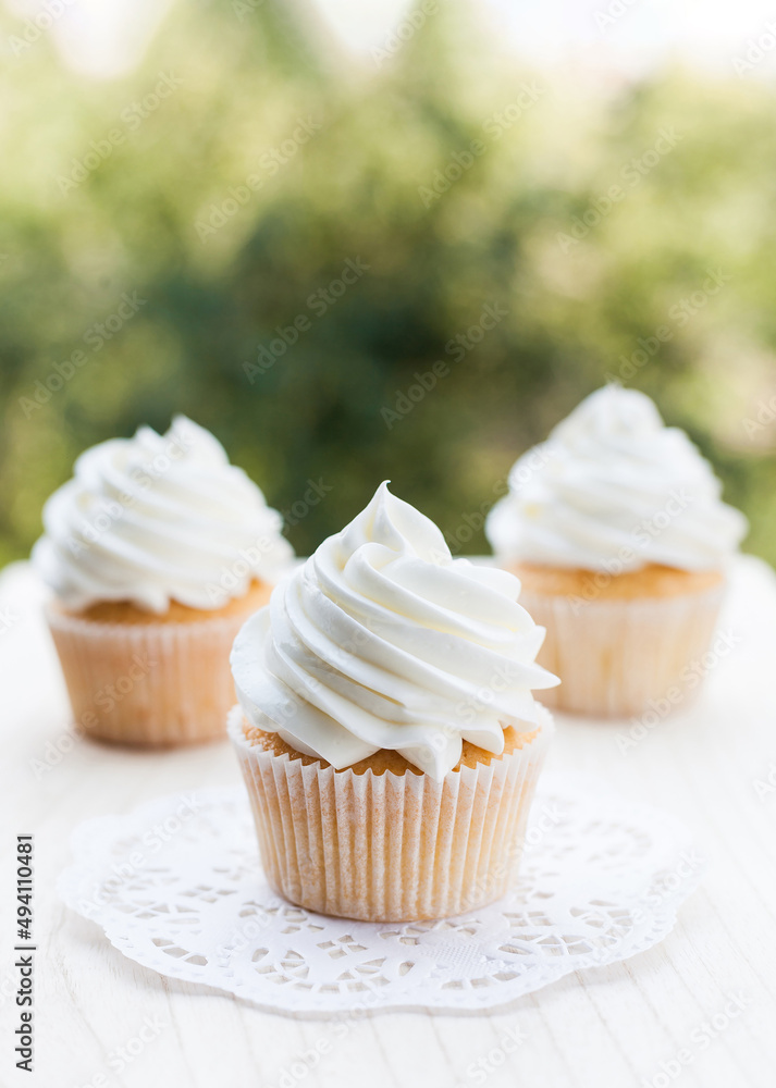 Vanilla cupcakes topped with swirl of sweet vanilla frosting captured on the table i a sunny day. Vanilla cupcakes topped with swirl of sweet vanilla frosting captured on the table i a sunny day.