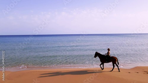 Aerial 4k women riding brown horse at natural sandy beach with crystal clear blue water and natural surrounding in Karpaz Peninsula, North Cyprus photo