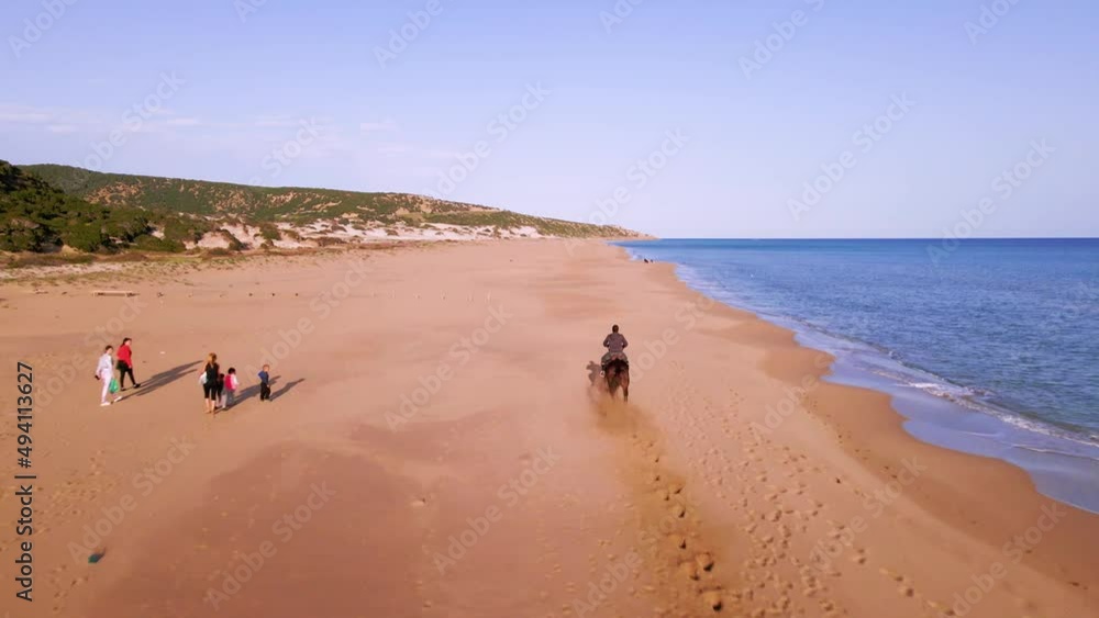 Aerial 4k man riding brown horse at natural sandy beach with crystal clear blue water and natural surrounding in Karpaz Peninsula, North Cyprus Aerial 4k man riding brown horse at natural sandy beach with crystal clear blue water and natural surrounding in Karpaz Peninsula, North Cyprus