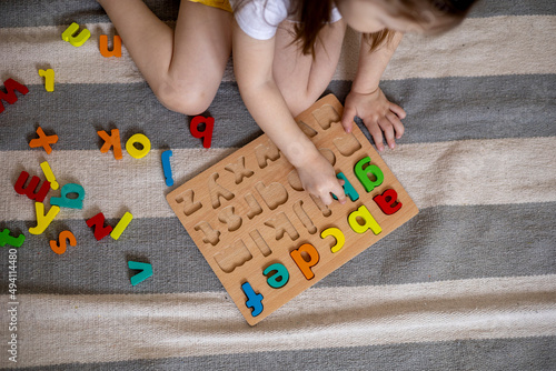 Top view of kids hands building words by using colored Montessori movable alphabet from the wooden tray on blackboard.