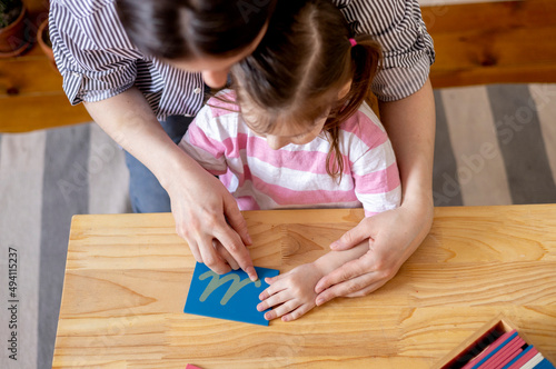 Montessori material. Mom helps her daughter learn letters using the rough alphabet.