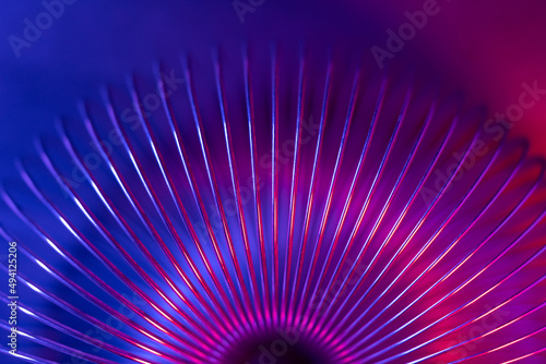 Closeup of coiled metal spring with sufficiently high strength and elastic properties in neon blue and red light. Macro photo, selective focus. photo