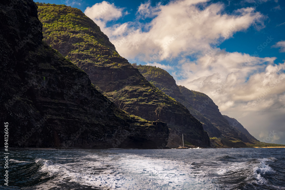 2022-03-21 RUGGED COASTLINE ALONE THE NA PALI COAST WITH WAVES AND AN ANCHORED SAIL BOAT AND CLOUDY SKY