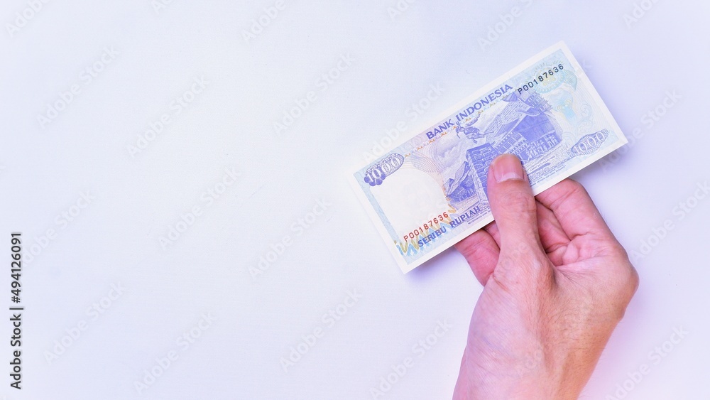 Indonesian Rupiah the official currency of Indonesia. Man's hand is making a payment. Male hand showing Indonesian Rupiah Note. Business Investment Economy and Finance Concept Uang 1000 1.000 Rupiah Indonesian Rupiah the official currency of Indonesia. Man's hand is making a payment. Male hand showing Indonesian Rupiah Note. Business Investment Economy and Finance Concept Uang 1000 1.000 Rupiah