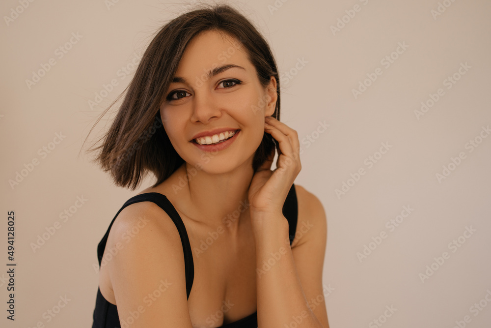Fototapeta premium Close-up of young caucasian woman with clean skin, natural makeup and white teeth on white background. Brunette girl with bob haircut looks at camera. Female beauty concept