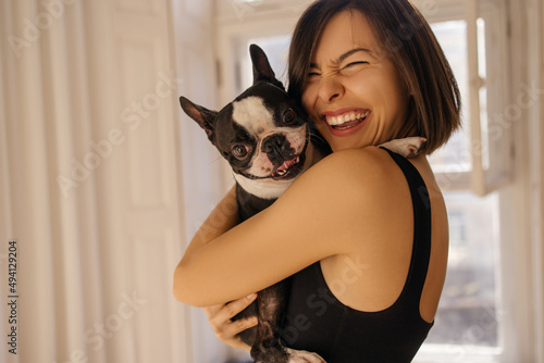 Cute young caucasian girl hugging funny bulldog dog with closed eyes. Brunette woman is enjoying good day and posing with her pet. Love for pets, joy and tenderness photo