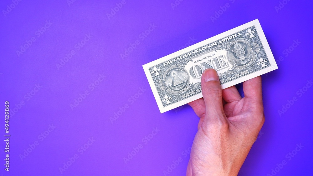 Businessman's hand holding American Dollar Banknotes, isolated on a purple background. Business Investment Economy Saving Loan Income Money and Finance concept. One Dollar, 1 USD. Prosperity concept. Businessman's hand holding American Dollar Banknotes, isolated on a purple background. Business Investment Economy Saving Loan Income Money and Finance concept. One Dollar, 1 USD. Prosperity concept.