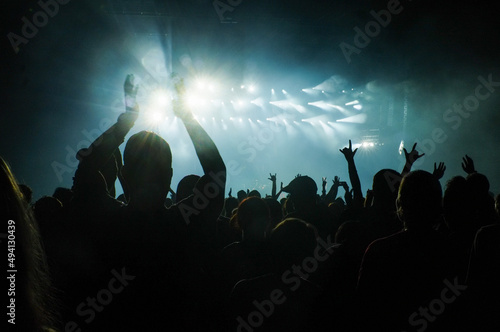 People in a crowd raise their hands in excitement at a concert with bright lights