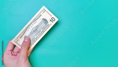 Man's hand is making a payment. Business Investment Economy Money Loan Saving Income and Finance concept. Male hand showing dollar bills on green background. Ten Dollar. 10 USD. Prosperity concept.