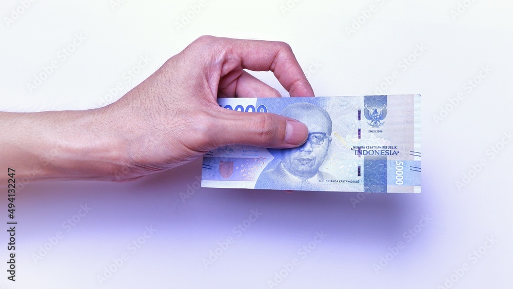 Indonesian Rupiah the official currency of Indonesia. Man's hand is making a payment. Male hand showing Indonesian Rupiah Note. Business Investment Economy and Finance Concept Uang 50000 50.000 Rupiah Indonesian Rupiah the official currency of Indonesia. Man's hand is making a payment. Male hand showing Indonesian Rupiah Note. Business Investment Economy and Finance Concept Uang 50000 50.000 Rupiah