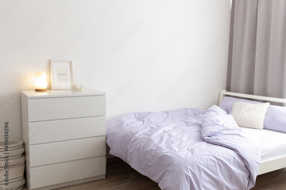 Bedroom in lilac color. Bed with purple linen white chest of