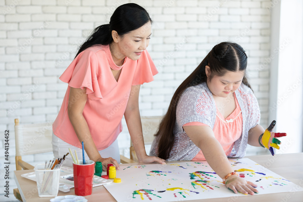 woman teacher and down syndrome girl with painted hands, drawing a picture on paper woman teacher and down syndrome girl with painted hands, drawing a picture on paper