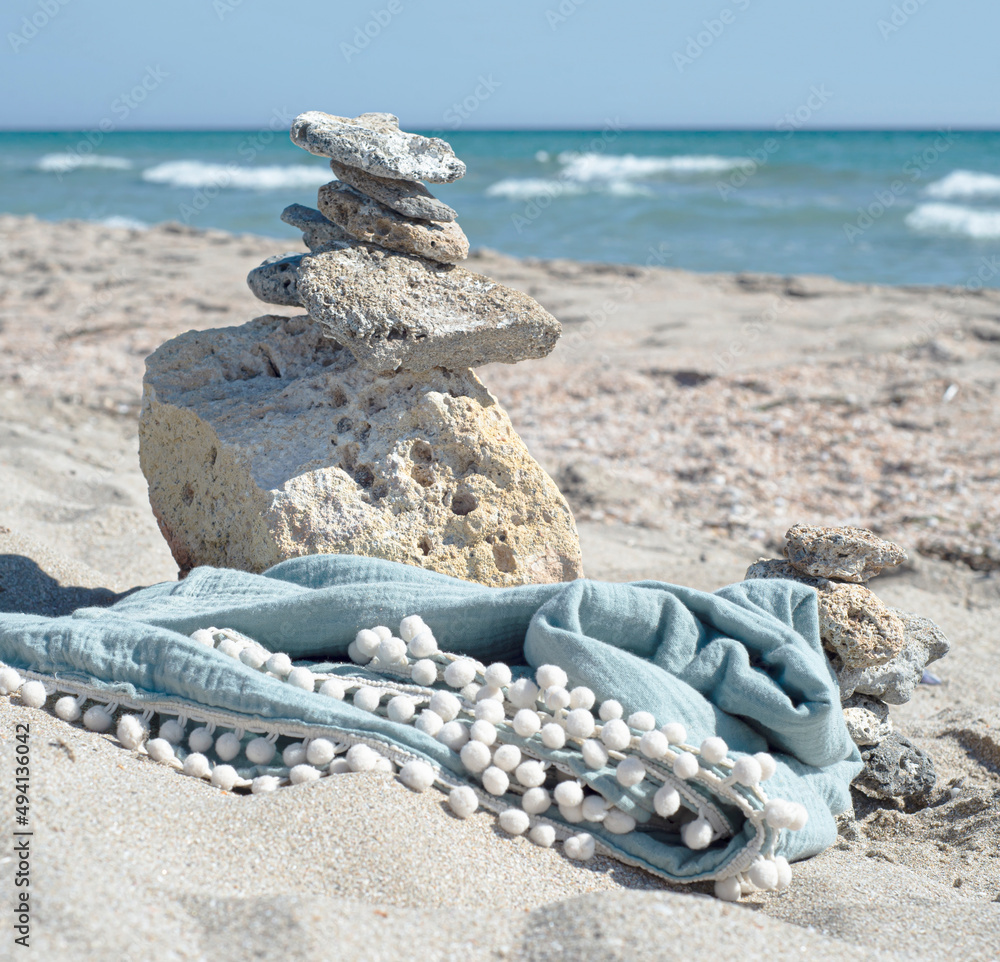 Muslin towel on the coast against the background of the sea. Organic body textiles and a tower of stones on a sandy beach.