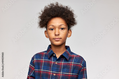 Id picture of handsome adorable dark-skinned boy of 12-years-old standing against cute studio wall with blank copy space for your advertising content, having afro haircut, dressed in stylish shirt © Anatoliy Karlyuk