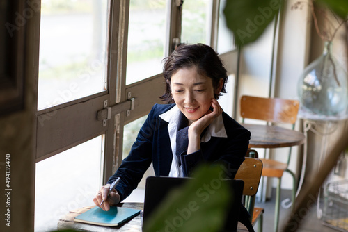 カフェでノートパソコンを見るミドル世代の日本人ビジネスウーマン