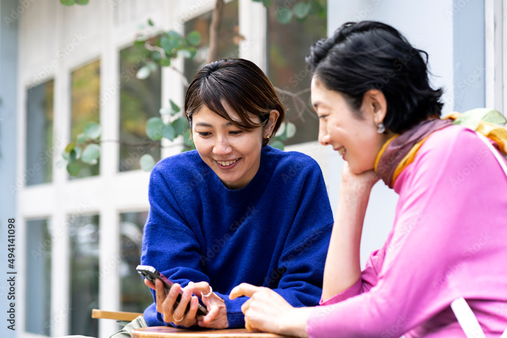 カフェテラスでスマートフォンを見るミドル世代の日本人女性2人 カフェテラスでスマートフォンを見るミドル世代の日本人女性2人